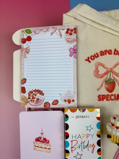 Strawberry and dessert-themed lined notepad with illustrated birthday cake greeting card and Joybars Happy Birthday milk chocolate in a birthday gift box