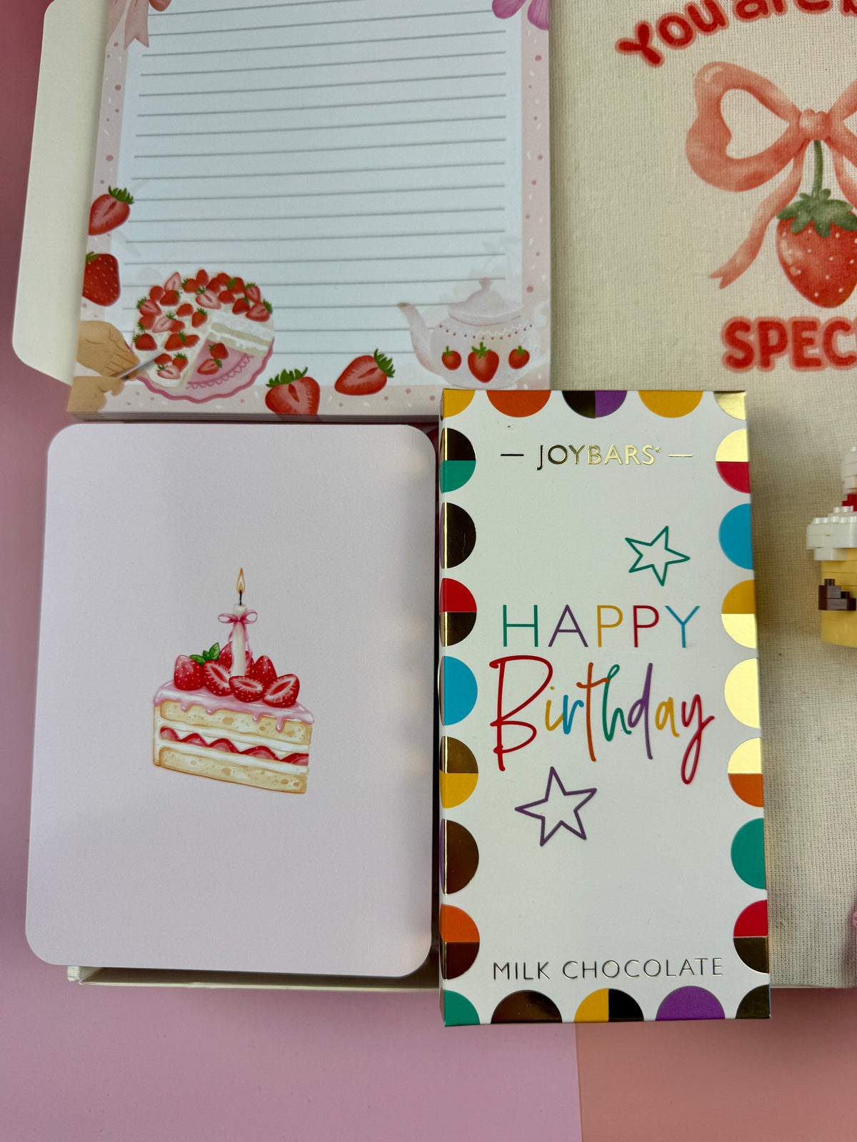 Strawberry and dessert-themed lined notepad with illustrated birthday cake greeting card and happy birthday chocolate and a tote bag