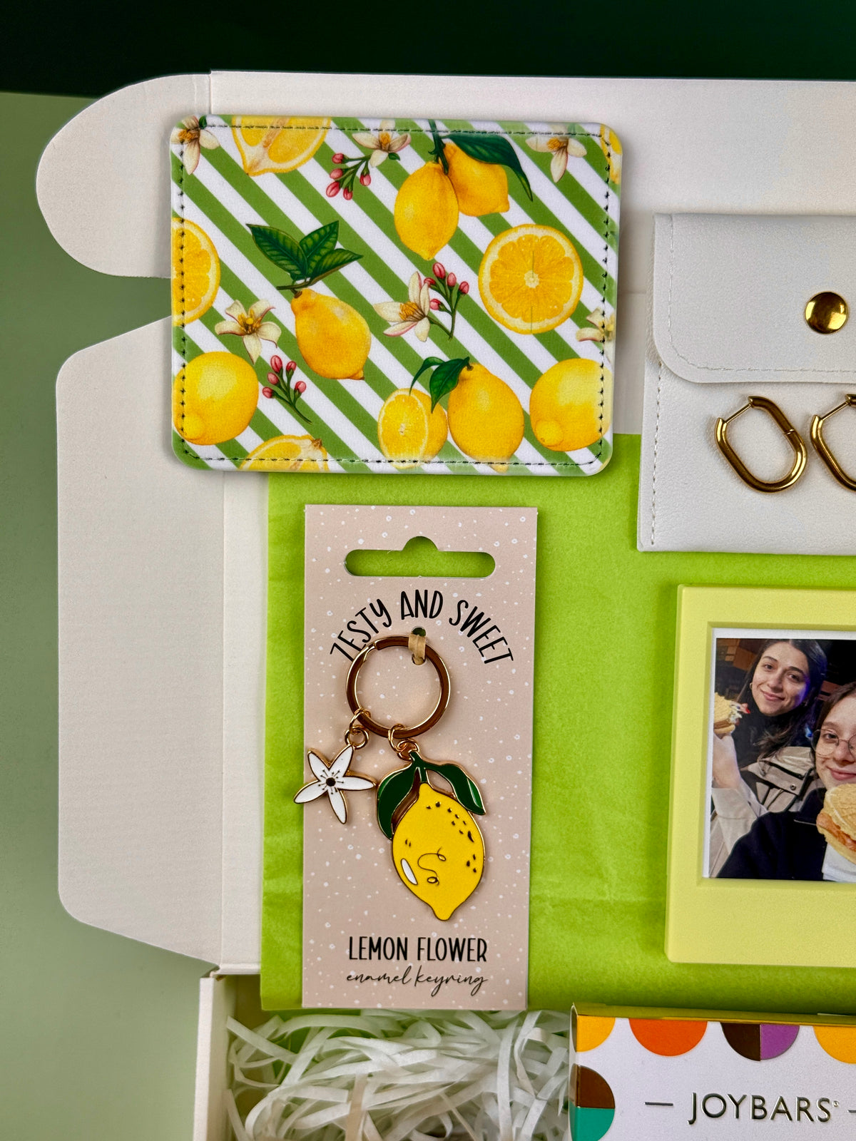 Close-up of lemon print card holder and lemon flower enamel keyring in a cheerful birthday gift box
 Copy