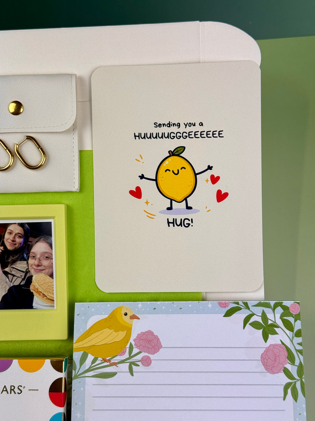 Cute lemon greeting card with Sending You a Hug message, pictured with gold earrings and floral notepad